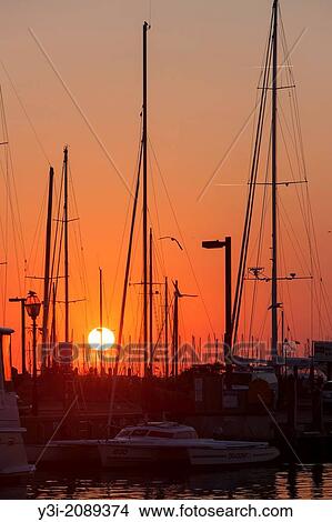 The rising sun turns the sky orange over sailboats and other pleasure craft docked in the harbor in Annapolis, Maryland. View Large Photo Image Picture - The rising sun turns the sky orange over sailboats and other pleasure craft docked in the harbor in Annapolis, Maryland.. Fotosearch