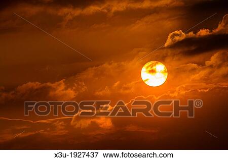 Stock Photo - The setting sun and clouds in the evening sky. Fotosearch