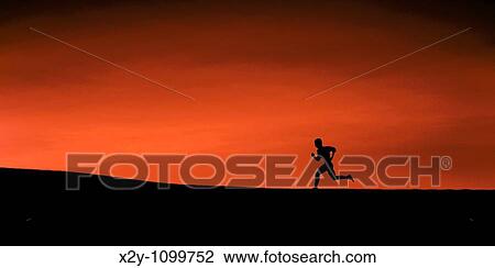 Stock Image - The silhouette of a man running up a slight incline, high contrast of land, figure and crimson sky. Fotosearch