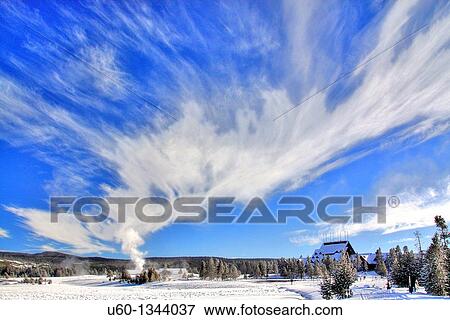 Stock Photo - The sky is filled with steam as Old Faithful Geyser erupts near The Old Faithful Inn during winter at Yellowstone National Park, Wyoming. Fotosearch