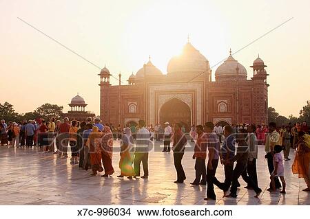Picture - The sun sets over the western Mosque as tourists wait in line on the marble floor to enter to inside of the Taj Mahal, Agra, India. Fotosearch