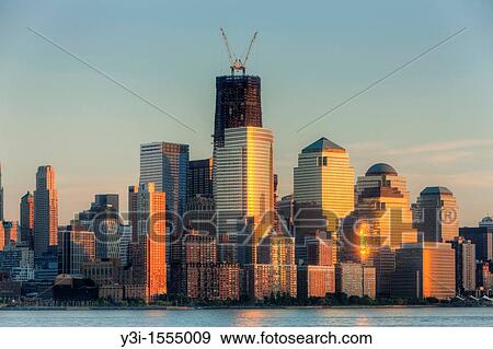 The sunset colored sky is reflected off of the building facades in lower Manhattan, including the World Financial Center and Battery Park City. The rising One World Trade Center Freedom Tower is in the background. View Large Photo Image Stock Photo - The sunset colored sky is reflected off of the building facades in lower Manhattan, including the World Financial Center and Battery Park City. The rising One World Trade Center Freedom Tower is in the background.. Fotosearch