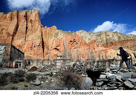 Stock Photograph - The village of Dhakmar and red cliff with caves. Nepal, Gandaki, Upper Mustang (near the border with Tibet). Model Released.. Fotosearch