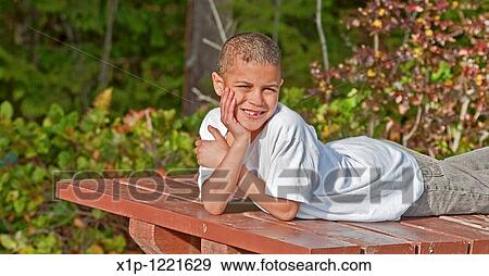 This 8 year old bi-racial boy is smiling outdoors in this portrait while lying on a picnic table with his hand on his face His missing teeth and bruised arm convey such a classic boyhood lifestyle View Large Photo Image Stock Photo - This 8 year old bi-racial boy is smiling outdoors in this portrait while lying on a picnic table with his hand on his face His missing teeth and bruised arm convey such a classic boyhood lifestyle. Fotosearch