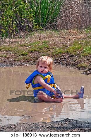This cute 18 month old Caucasian toddler girl is sitting in her diaper and life vest in a mud puddle and playing as she's taking off her sandal Great classic childhood summertime moment Background intentionally blurred to emphasize subject View Large Photo Image Stock Image - This cute 18 month old Caucasian toddler girl is sitting in her diaper and life vest in a mud puddle and playing as she's taking off her sandal Great classic childhood summertime moment Background intentionally blurred to emphasize subject. Fotosearch