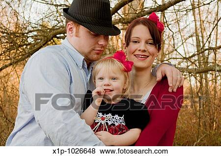 This cute young family is a father embracing his wife and young daughter and they are both wearing red bows in their hair Background is intentionally blurred for artistic effect View Large Photo Image Stock Photo - This cute young family is a father embracing his wife and young daughter and they are both wearing red bows in their hair Background is intentionally blurred for artistic effect. Fotosearch