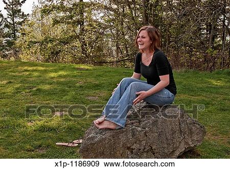 This image is a young Caucasian woman wearing blue jeans and a black shirt, laughing while sitting barefoot on a large rock Very natural looking, outdoors portrait View Large Photo Image Stock Photo - This image is a young Caucasian woman wearing blue jeans and a black shirt, laughing while sitting barefoot on a large rock Very natural looking, outdoors portrait. Fotosearch