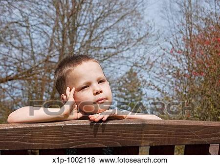 Stock Photo - This little boy has an expression as tho dreaming for summer with the bare branches of early spring in the background Background is intentionally blurred for artistic effect. Fotosearch