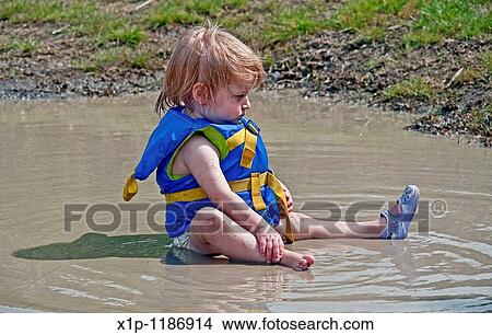 This little toddler girl is wearing a blue life vest and sitting in a mud puddle with a serious expression on her face She's in her diaper also and has one plastic shoe on and one off Darling summertime photo View Large Photo Image Picture - This little toddler girl is wearing a blue life vest and sitting in a mud puddle with a serious expression on her face She's in her diaper also and has one plastic shoe on and one off Darling summertime photo. Fotosearch