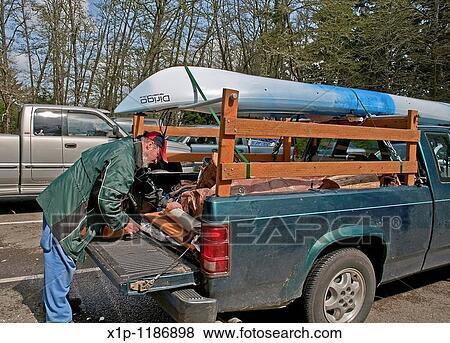 This middle aged Caucasian man is preparing the back of his truck with camping gear with a kayak loaded on top in readiness for a camping trip View Large Photo Image Stock Photo - This middle aged Caucasian man is preparing the back of his truck with camping gear with a kayak loaded on top in readiness for a camping trip. Fotosearch