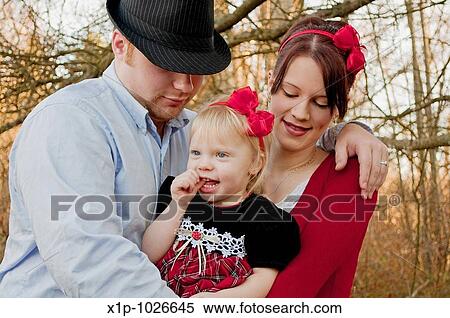 This photo is a small young family with mother, father and toddler girl, mom and daughter are wearing red bows while dad embraces both Background is intentionally blurred for artistic effect View Large Photo Image Stock Photography - This photo is a small young family with mother, father and toddler girl, mom and daughter are wearing red bows while dad embraces both Background is intentionally blurred for artistic effect. Fotosearch