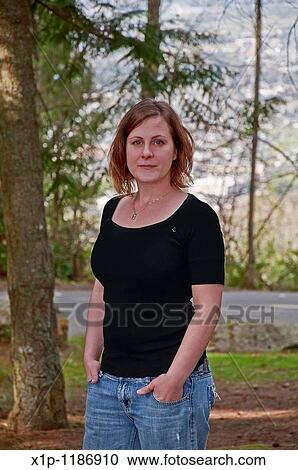 This portrait is a natural looking young Caucasian woman in her twenties wearing a black shirt and blue jeans in a casual outdoor setting Background is intentionally blurred to emphasize subject View Large Photo Image Stock Image - This portrait is a natural looking young Caucasian woman in her twenties wearing a black shirt and blue jeans in a casual outdoor setting Background is intentionally blurred to emphasize subject. Fotosearch