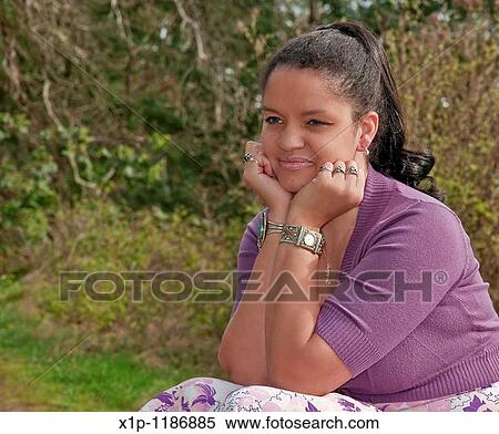 Stock Photography - This portrait is a pretty multri racial woman in her thirties with her face resting on her hands as she's sitting outdoors Her facial expression is one of dreaming, contemplative, thinking She's wearing a lavender shrug. Fotosearch