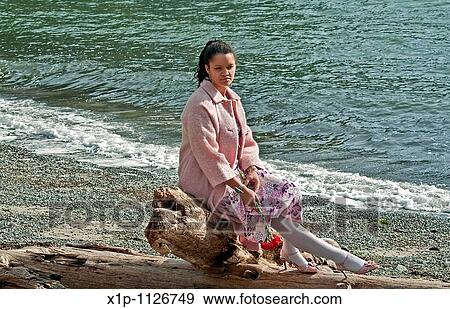This pretty multi ethnic woman conveys many emotions, sadness, dejected, lonely as she's sitting on driftwood at a beach, with some red carnation flowers hanging down, as if she as lost love View Large Photo Image Stock Photo - This pretty multi ethnic woman conveys many emotions, sadness, dejected, lonely as she's sitting on driftwood at a beach, with some red carnation flowers hanging down, as if she as lost love. Fotosearch