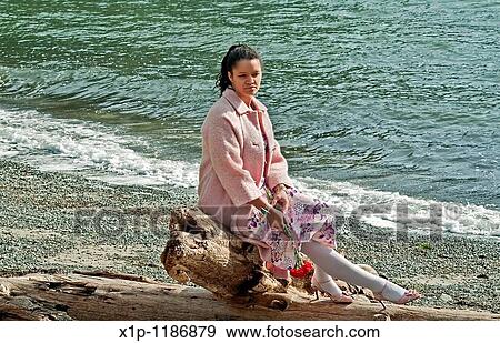 This pretty multi ethnic woman conveys many emotions, sadness, dejected, lonely as she's sitting on driftwood at a beach, with some red carnation flowers hanging down, as if she as lost love View Large Photo Image Stock Photo - This pretty multi ethnic woman conveys many emotions, sadness, dejected, lonely as she's sitting on driftwood at a beach, with some red carnation flowers hanging down, as if she as lost love. Fotosearch