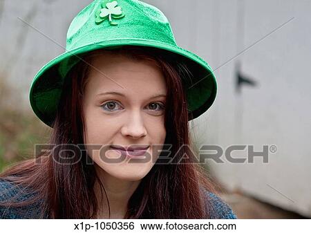 Stock Photograph - This pretty young woman has long brunette hair and a gentle smile with big brown eyes She's wearing a green clover hat in celebration of St Patricks? Day. Fotosearch