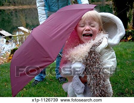 This two year old Caucasian toddler girl is crying outside under a burgundy colored umbrella She's wearing a white coat and white furry scarf and holding her stuffed toy dog Lots of emotion in this image View Large Photo Image Stock Photo - This two year old Caucasian toddler girl is crying outside under a burgundy colored umbrella She's wearing a white coat and white furry scarf and holding her stuffed toy dog Lots of emotion in this image. Fotosearch