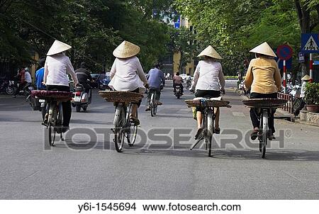 Picture - Thre women in conical hats on bicycles Hanoi Vietnam. Fotosearch
