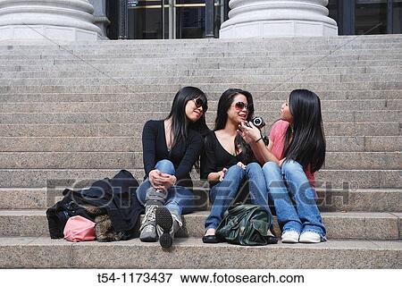 Three Asian woman sitting on the steps of New Yorks main post office and looking at photos View Large Photo Image Stock Photo - Three Asian woman sitting on the steps of New Yorks main post office and looking at photos. Fotosearch