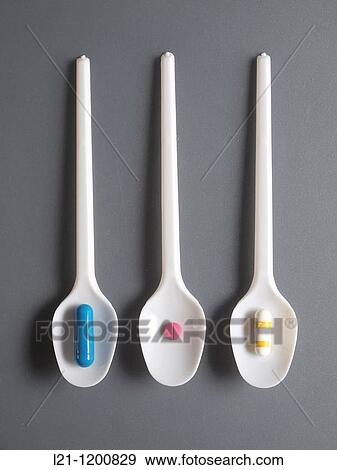 Stock Photo - Three blue, red and yellow pills in white spoons on gray background. Fotosearch
