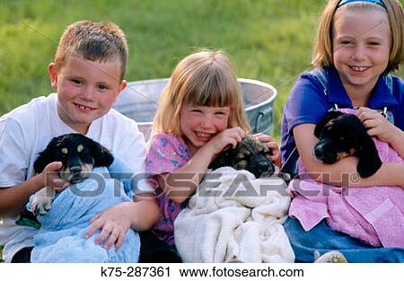 Stock Image - Three children and their puppies. Fotosearch