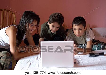 Three children lying on a bed using a laptop, France View Large Photo Image Picture - Three children lying on a bed using a laptop, France. Fotosearch