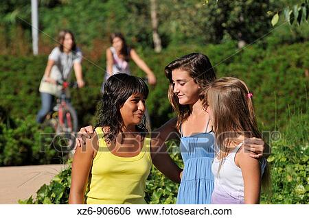 three friends talking in the foreground, while two more arrive on a bicycle View Large Photo Image Stock Photograph - three friends talking in the foreground, while two more arrive on a bicycle. Fotosearch
