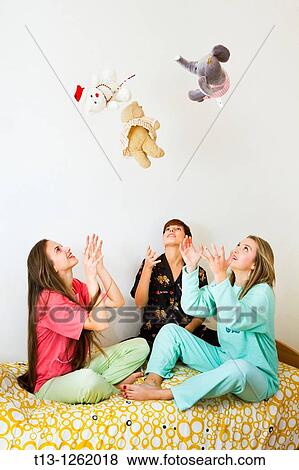 Stock Photo - Three girls are playing with stuffed dolls, throwing them upwards. Fotosearch