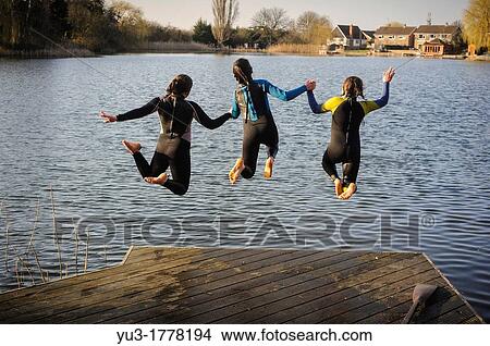 Three girls jumping into a lake while holding hands, England, UK View Large Photo Image Picture - Three girls jumping into a lake while holding hands, England, UK. Fotosearch