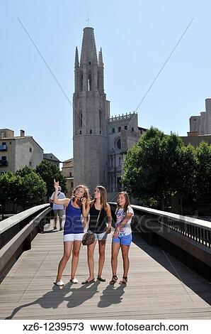 Stock Image - Three girls pointing in a bridge, Sant Felix church is in the background, Girona, Catalonia, Spain, Europe. Fotosearch