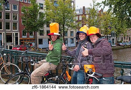 Picture - Three loyal Dutch soccer fans with Dutch hats by river canals in Amsterdam Holland Netherlands downtown city. Fotosearch