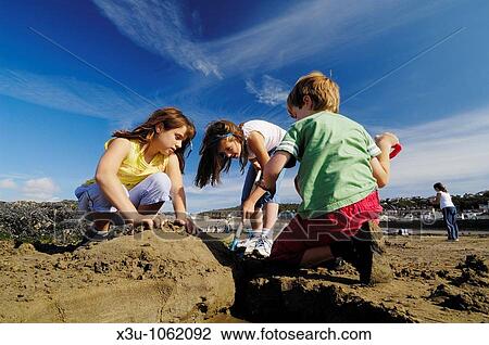 Stock Image - Three preteen children playing in the sun on the beach at Westward Ho in Devon England. Fotosearch