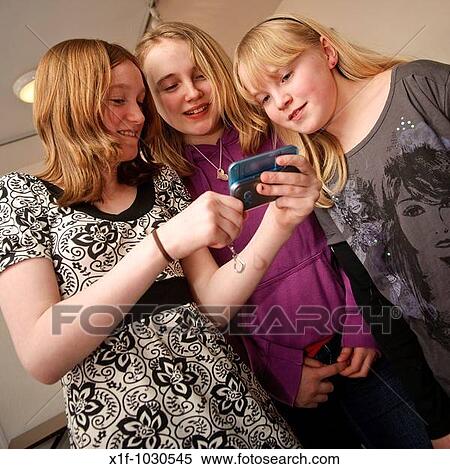 Stock Photography - Three teenage girls reading a text message together on a mobile phone, UK. Fotosearch