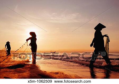 Stock Photo - Three women in traditional hats on Mui Ne Beach, Vietnam Fishing at sunrise. Fotosearch