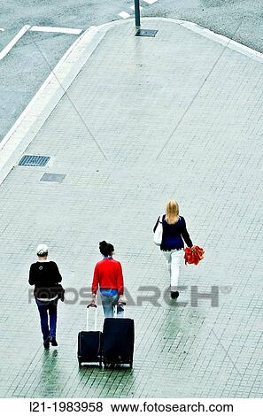 Three women on a wet sidewalk. Woman walking, woman dragging two bags, woman holding an orange umbrella. Barcelona, Catalonia, Spain. View Large Photo Image Stock Photo - Three women on a wet sidewalk. Woman walking, woman dragging two bags, woman holding an orange umbrella. Barcelona, Catalonia, Spain.. Fotosearch