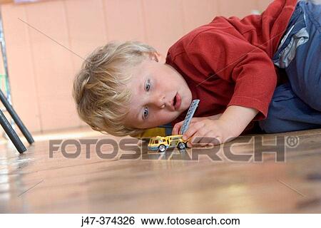 Stock Photograph - Three year old boy, lying on the floor at nursrey school, playing with a toy car. Fotosearch