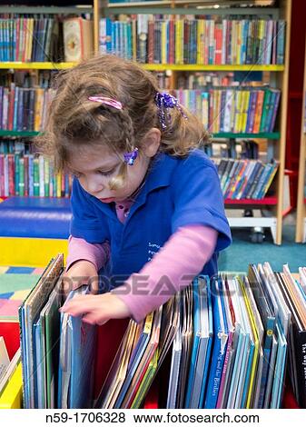 Stock Photo - Three year old caucasian girl in preschool top looking at books in a public library.. Fotosearch
