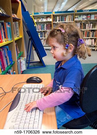 Stock Photograph - Three year old caucasian girl in preschool top using a computer in a public library.. Fotosearch