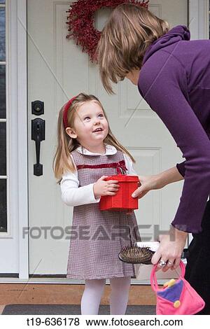 Stock Photo - Three year old girl being handed a red box from her mother on the porch of their house. Fotosearch