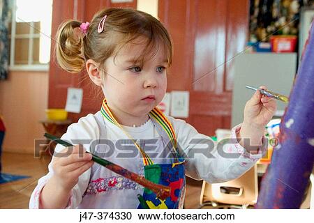 Three year old girl, painting at nursrey school, with an apron on, concentrating. Standing at an easel View Large Photo Image Stock Image - Three year old girl, painting at nursrey school, with an apron on, concentrating. Standing at an easel. Fotosearch