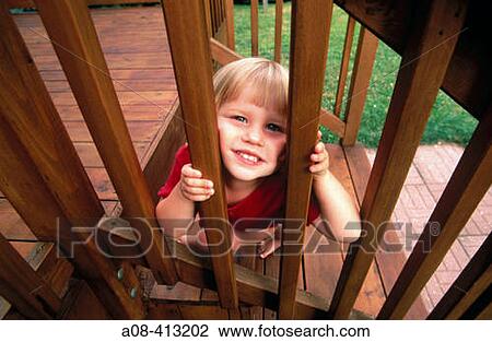 Stock Image - Three year old girl peers through railing spindles. USA.. Fotosearch