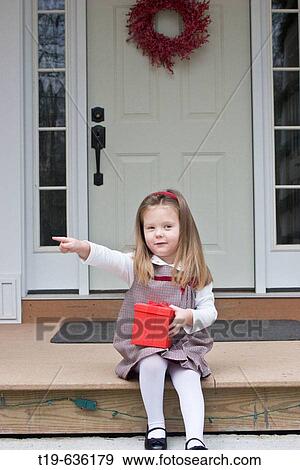 Three year old girl sitting on the porch of her family's house in Woodstock, CT, holding a Christmas present. USA View Large Photo Image Stock Photo - Three year old girl sitting on the porch of her family's house in Woodstock, CT, holding a Christmas present. USA. Fotosearch