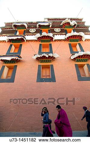 Stock Image - Tibetan pilgrims and a monk walking by one of Labrang monastery complex temples.. Fotosearch