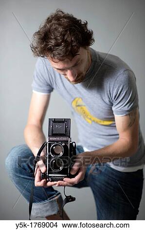 Picture - Tilburg, Netherlands. Man with a vintage medium format twin lens reflex camera. Studio-portrait against grey background.. Fotosearch