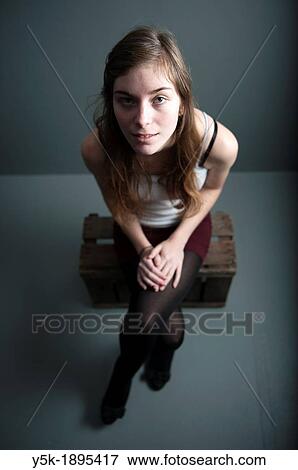 Tilburg, Netherlands. Studio-portrait of a young woman, against a grey background, seated on a wooden fruit crate. View Large Photo Image Stock Photo - Tilburg, Netherlands. Studio-portrait of a young woman, against a grey background, seated on a wooden fruit crate.. Fotosearch