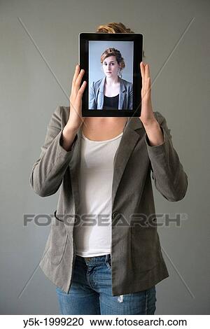 Tilburg, Netherlands. Young woman holding up an Digital Tablet, showing her portrait, which was taken earlier, in front of her face. View Large Photo Image Stock Image - Tilburg, Netherlands. Young woman holding up an Digital Tablet, showing her portrait, which was taken earlier, in front of her face.. Fotosearch