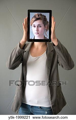 Tilburg, Netherlands. Young woman holding up an Digital Tablet, showing her portrait, which was taken earlier, in front of her face. View Large Photo Image Stock Image - Tilburg, Netherlands. Young woman holding up an Digital Tablet, showing her portrait, which was taken earlier, in front of her face.. Fotosearch
