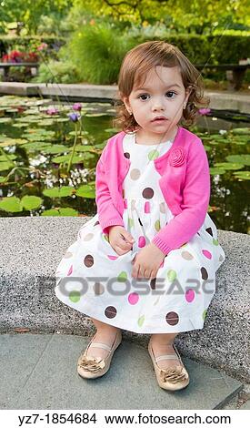 Toddler girl sitting looking into camera in garden View Large Photo Image Picture - Toddler girl sitting looking into camera in garden. Fotosearch