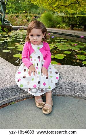 Stock Image - Toddler girl sitting looking into camera in garden. Fotosearch