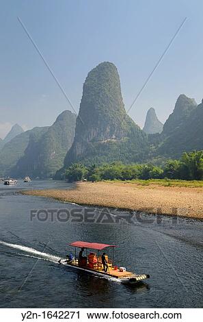 Tour boat raft traveling down the Li river with tall karst mountain cones in background. Guangxi, China. View Large Photo Image Stock Image - Tour boat raft traveling down the Li river with tall karst mountain cones in background. Guangxi, China.. Fotosearch